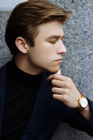 portrait of an attractive young man in a blue suit in the city on gray background.watch on hand, gold wrist watch.pensiveの写真素材