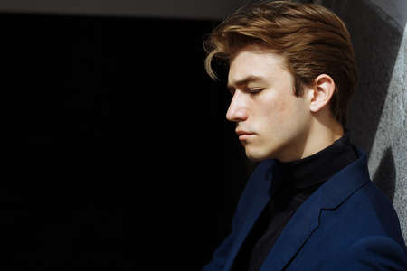 portrait of an attractive young man in a blue suit in the city on gray background.watch on hand, gold wrist watch.pensiveの写真素材