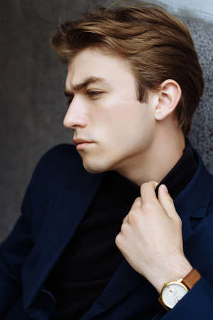 portrait of an attractive young man in a blue suit in the city on gray background.watch on hand, gold wrist watch.pensiveの写真素材