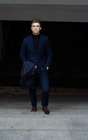 portrait of attractive young man in blue suit with coat in hand on black backgroundの写真素材