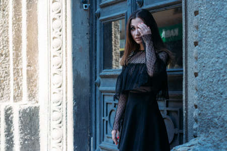 portrait of a beautiful girl, a brunette girl in a black dress, stands near a big black door, goes into it. a new stage in life, enterの写真素材