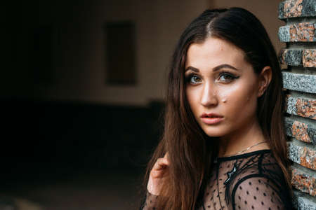 Emotional portrait of Fashion stylish portrait of pretty young woman. city portrait. sad girl. brunette in a black dress with stars and planets on a dress. expectation. dreams. stands near the wallの写真素材