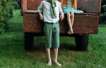 a barefooted girl in a green dress is sitting in an old caravan, and beside her, barefoot, on the grass, stands a guy in a white shirt and green pants, with a green sweater tied in front.farming life of adolescents. friendship in the summer.の写真素材