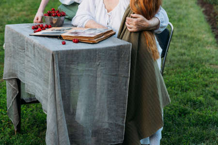 grandmother with her grandchildren sitting in a chair at the table on which the cherry is lying, in...