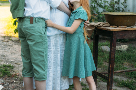 meeting grandmother and grandchildren. grandmother embraces grandchildren, brother and sister. grandson and granddaughter came to visit. give flowers. relatives meeting. Grandmother in white vintage clothing and grandchildren in green clothes. next to it there is a table on which lie clothes for washing by handsの写真素材