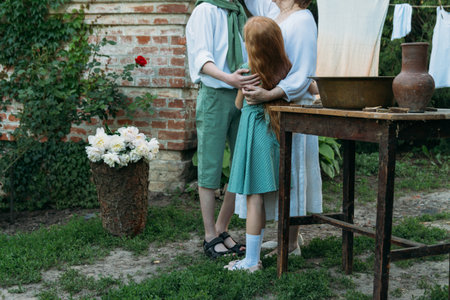 meeting grandmother and grandchildren. grandmother embraces grandchildren, brother and sister. grandson and granddaughter came to visit. give flowers. relatives meeting. Grandmother in white vintage clothing and grandchildren in green clothes. next to it there is a table on which lie clothes for washing by handsの写真素材