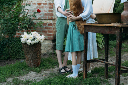 meeting grandmother and grandchildren. grandmother embraces grandchildren, brother and sister. grandson and granddaughter came to visit. give flowers. relatives meeting. Grandmother in white vintage clothing and grandchildren in green clothes. next to it there is a table on which lie clothes for washing by handsの写真素材