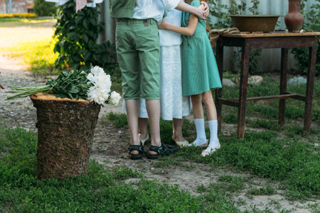 meeting grandmother and grandchildren. grandmother embraces grandchildren, brother and sister. grandson and granddaughter came to visit. give flowers. relatives meeting. Grandmother in white vintage clothing and grandchildren in green clothes. next to it there is a table on which lie clothes for washing by handsの写真素材