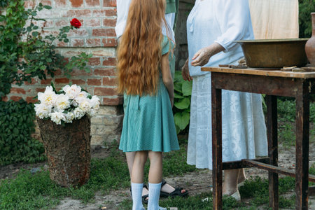 meeting grandmother and grandchildren. grandmother embraces grandchildren, brother and sister. grandson and granddaughter came to visit. give flowers. relatives meeting. Grandmother in white vintage clothing and grandchildren in green clothes. next to it there is a table on which lie clothes for washing by handsの写真素材