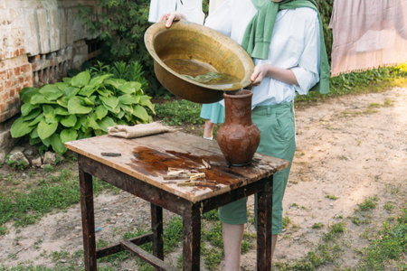a boy in a white shirt and a green sweater, holds a clay jug, pours water out of it into a copper basin. help, countryside. village.の写真素材
