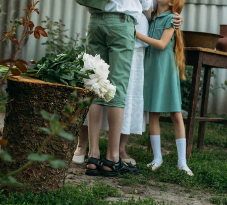 meeting grandmother and grandchildren. grandmother embraces grandchildren, brother and sister. grandson and granddaughter came to visit. give flowers. relatives meeting. Grandmother in white vintage clothing and grandchildren in green clothes. next to it there is a table on which lie clothes for washing by handsの写真素材