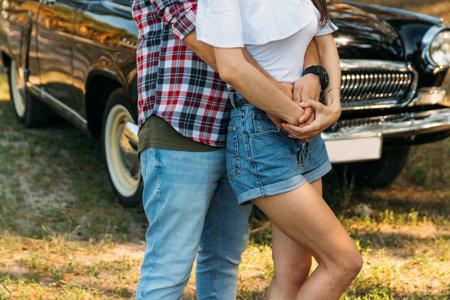 the guy is behind and hugs the girl, hands together. behind is a black car.holding hands in the summer. on the hand of a guy wearing a black watch. date in summerの写真素材