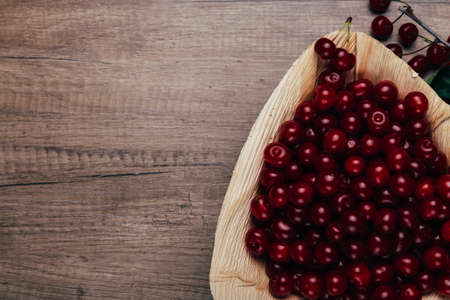 fresh red cherries in a wooden plate on a wooden table. wooden plate on a wooden background. next to...