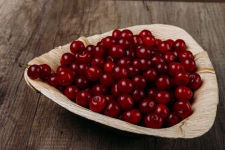 fresh red cherries in a wooden plate on a wooden table. wooden plate on a wooden background. a plate in the form of a triangle. ecology. proper nutrition. summer giftsの写真素材