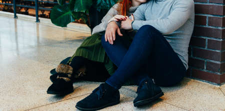 the couple is sitting on the floor in an embrace. embrace. a female hand with a ring, a man's hand with a watch. talking. gray sweaters. Kiss on my cheek.black boots with furの写真素材
