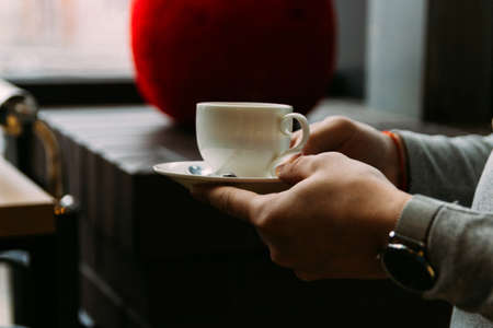 Men's hands in a gray sweater hold a white cup of coffee.の写真素材