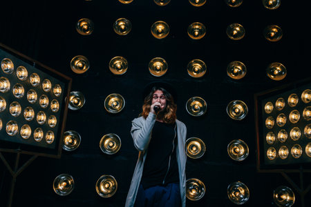 men singer with microphone on the stage, with long hair, against the background of bright lanterns, sceneの写真素材