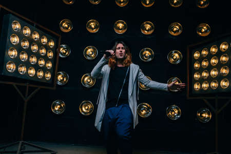 men singer with microphone on the stage, with long hair, against the background of bright lanterns, sceneの写真素材
