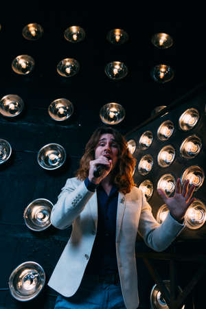 men singer with microphone on the stage, with long hair, against the background of bright lanterns,...