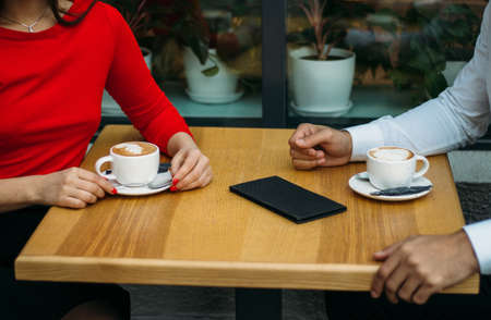 a couple, two, a guy and a girl are sitting in a cafe, drinking coffee, two cups of cappuccino on the table, bill for a drink.discussionの写真素材