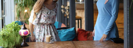 meeting two women in a cafe for coffee. one stood up to greet the second. blue dress, dress in a flower, on a carved table is a cup of coffee and a lamp. business discussion.の写真素材