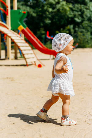 portrait of a little girl in a white dress and white hat with flowers on the background on the playground, a child in the city in the summer.running around the siteの写真素材