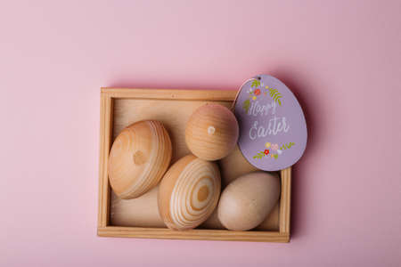 wooden eggs, blanks for dyeing eggs, for pascuka, lie in a wooden box. next to it is a plate in the shape of a purple color with the inscription, happy hour.pink backgroundの写真素材