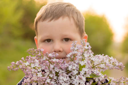 portrait of a boy with lilac.bouquet of purple lilac in children's hands. hands holding a purple...