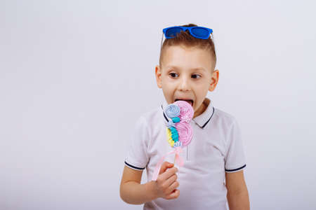 a boy in sunglasses, denim shorts and a white T-shirt, on a white background holds a candy in the form of a figure eight. Women's day, congratulations. men congratulate. March 8の写真素材