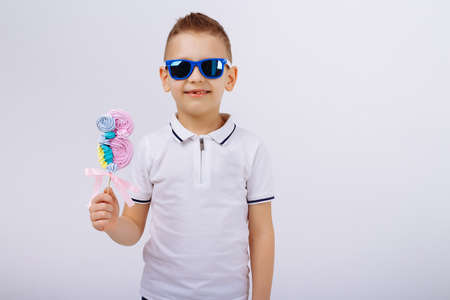 a boy in sunglasses, denim shorts and a white T-shirt, on a white background holds a candy in the form of a figure eight. Women's day, congratulations. men congratulate. March 8の写真素材