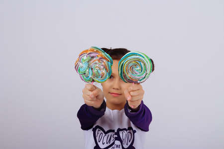 A girl holds in two hands multicolored candies on a stick, showing them to the camera. sweet life. childhood with sweetsの写真素材