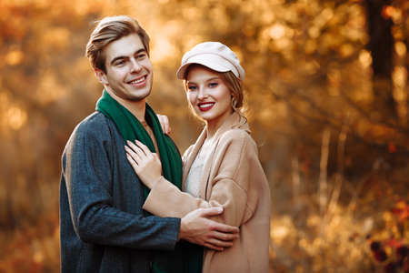 guy and girl are embracing and smiling while looking at the camera, a beige cap and a green scarf, autumn. date of a happy and loving coupleの写真素材