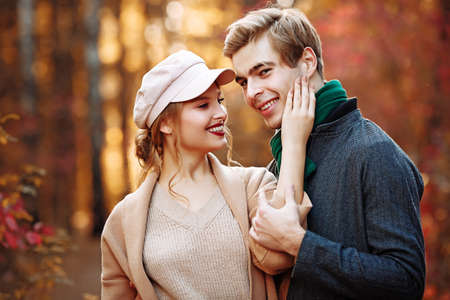 happy, couple in love hugs and smiles on the street, autumn, green scarf and cap, beige coat. man and woman on a date, valentines day. walk in the parkの写真素材