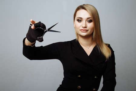 young woman with beautiful blonde hair look at scissors in one hand studio shot gray background cut bad hair, short cutの写真素材