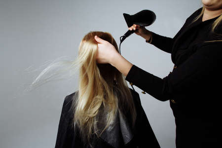portrait of a girl Hairdresser dries hair with a hairdryer in beauty salon. girl dries hair blonde hair, winding them on a comb. dryer blows on hair.の写真素材