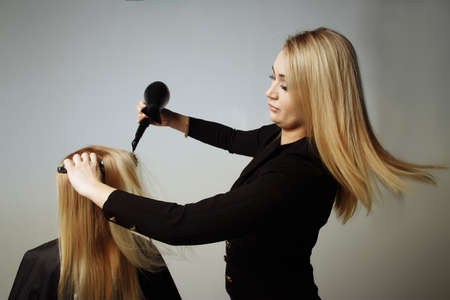 portrait of a girl Hairdresser dries hair with a hairdryer in beauty salon. girl dries hair blonde hair, winding them on a comb. dryer blows on hair.の写真素材