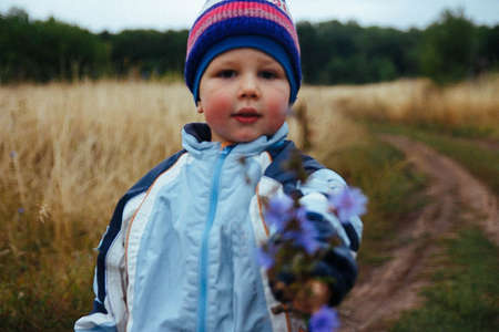 stands on the road in the field and holds flowers to the camera, gift, holiday, mother's day, smileの写真素材