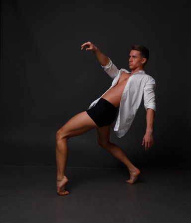 white man in an unbuttoned white shirt and black shorts dancing on a gray background, bare legs and torso, studio shotの写真素材
