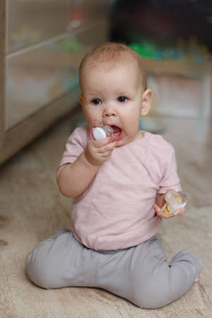 Little girl with other. little baby with a pacifier. in a pink sweater and gray pants sits on the floor. in the second hand holds a pacifierの写真素材