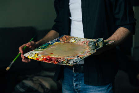 the artist holds a palette with paints and a brush. a man in jeans and a black shirt. hobbyの写真素材
