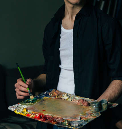 man in jeans, artist, artist brush mix color oil painting on palette is holding in his hand closeupの写真素材