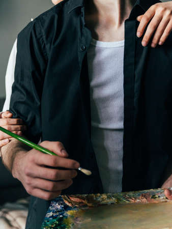 a man holds in his hand a palette with paints and a brush, and behind him they embrace. supportの写真素材