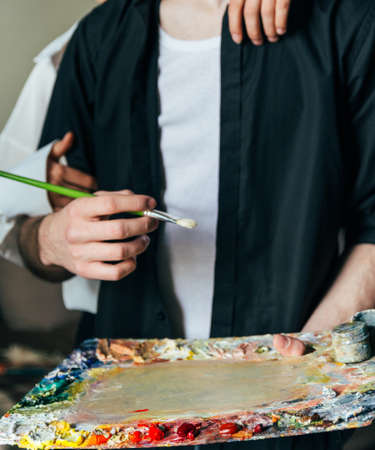 a man holds in his hand a palette with paints and a brush, and behind him they embrace. supportの写真素材