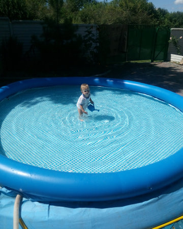 a small child sits in the pool and smiles, plays, the sun shines summerの写真素材