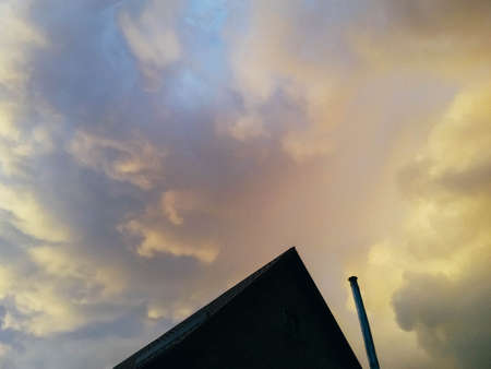 yellow-pink clouds hanging over the roof of the houseの写真素材
