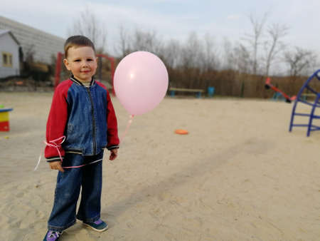 little boy with a balloon pink, smiles, standing on the street in the sandの写真素材