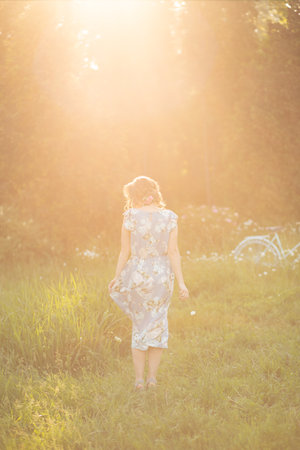 portrait of a beautiful girl at sunset in summer in a field with a flower in her hand, walks in the summer, goes, the sun is shining, summer walk relaxation field and flowersの写真素材