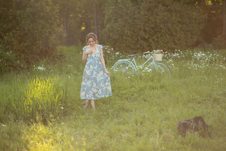 portrait of a beautiful girl at sunset in summer in a field with a flower in her hand, walks in the summer, goes, the sun is shining, summer walk relaxation field and flowersの写真素材