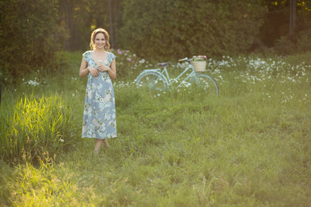 portrait of a beautiful girl at sunset in summer in a field with a flower in her hand, walks in the summer, goes, the sun is shining, summer walk relaxation field and flowersの写真素材