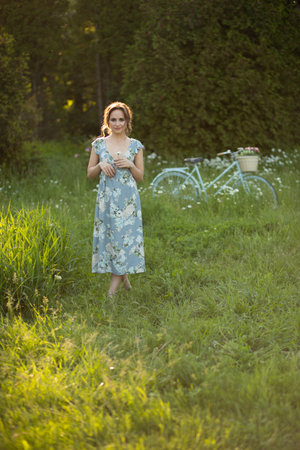 portrait of a beautiful girl at sunset in summer in a field with a flower in her hand, walks in the summer, goes, the sun is shining, summer walk relaxation field and flowersの写真素材